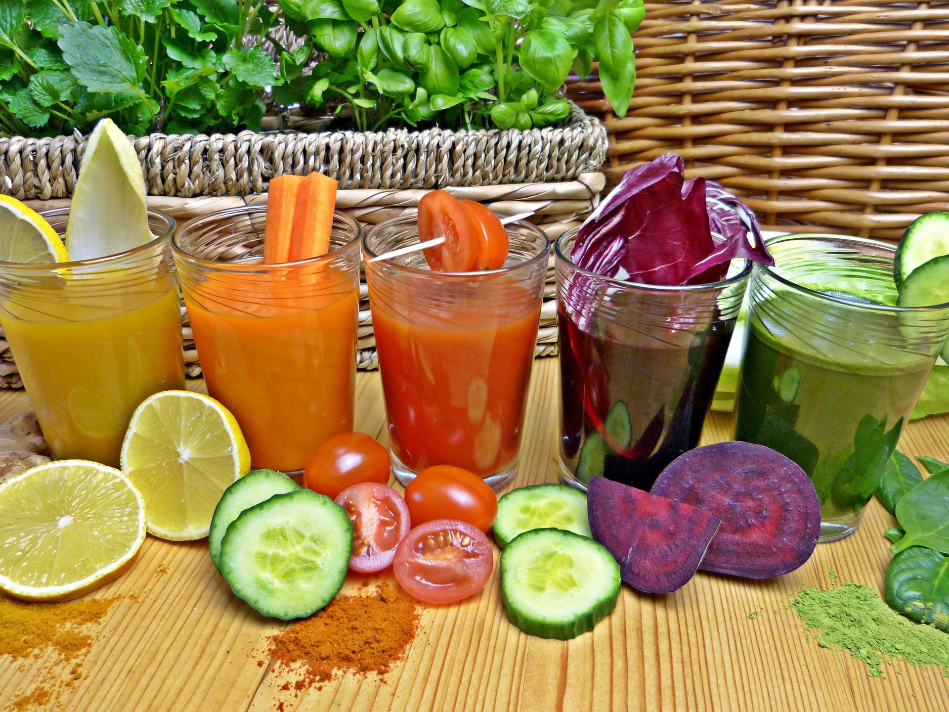 Cinq verres de jus de légumes limpides, agrume, carotte, tomate, betterave et vert, entourés de concombre et de tomates cerises