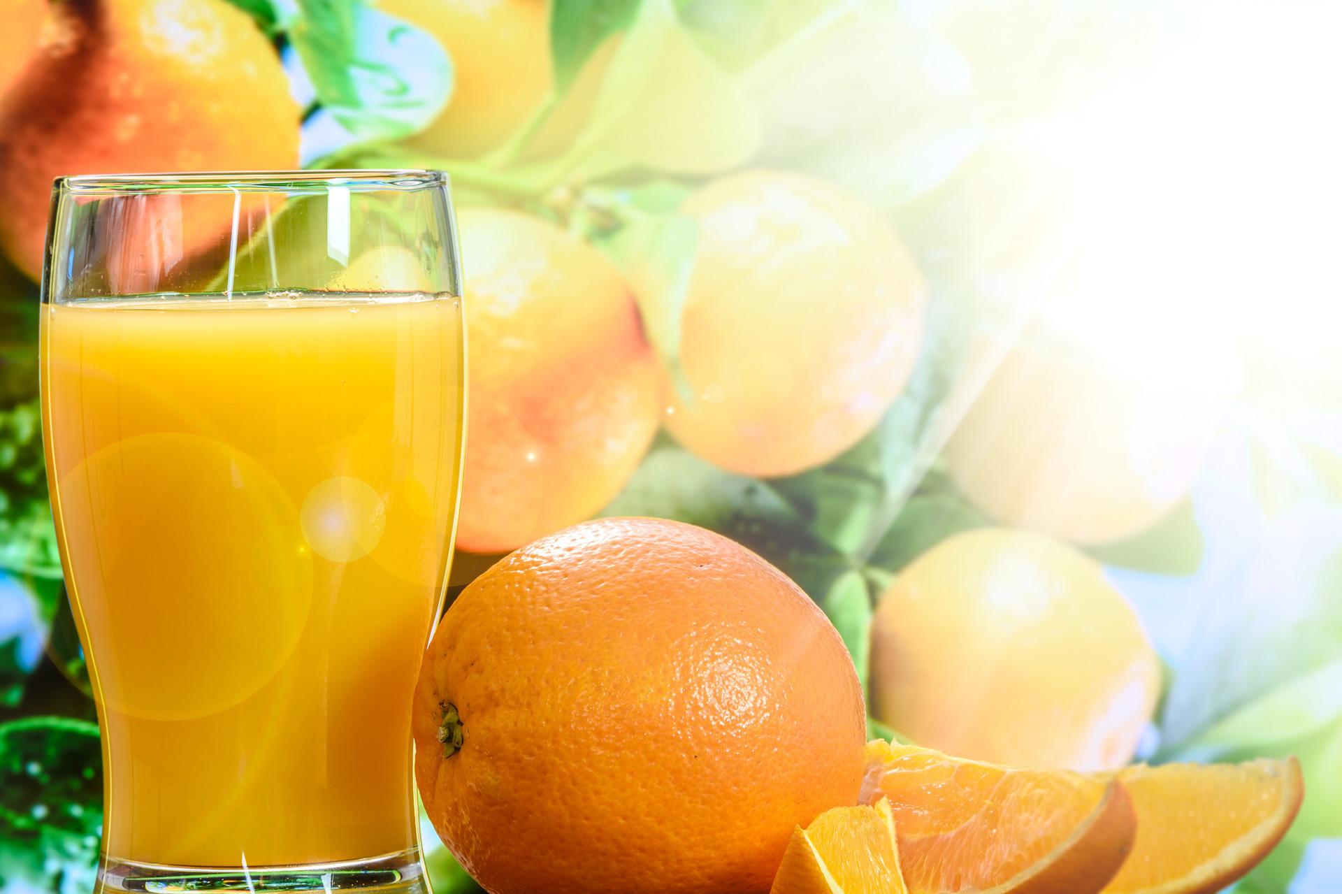 Grand verre de jus d'orange frais posé devant des oranges entières et des quartiers coupés, dans une lumière de contre-jour