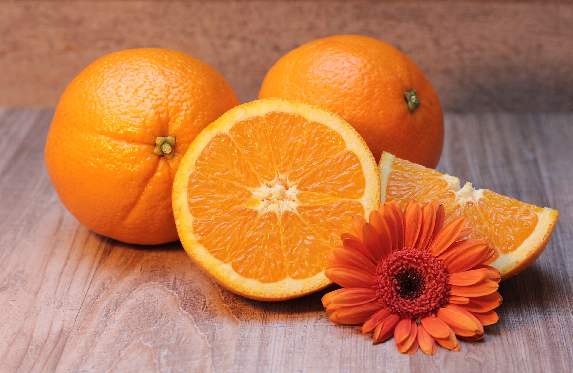 Deux oranges entières près d'une demi-orange coupée laissant voir sa chair et son cœur blanc
