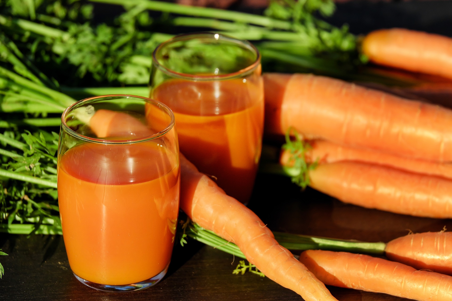 Deux verres de jus de carotte posés sur une table sombre à côté de carottes fraîches avec leurs fanes vertes