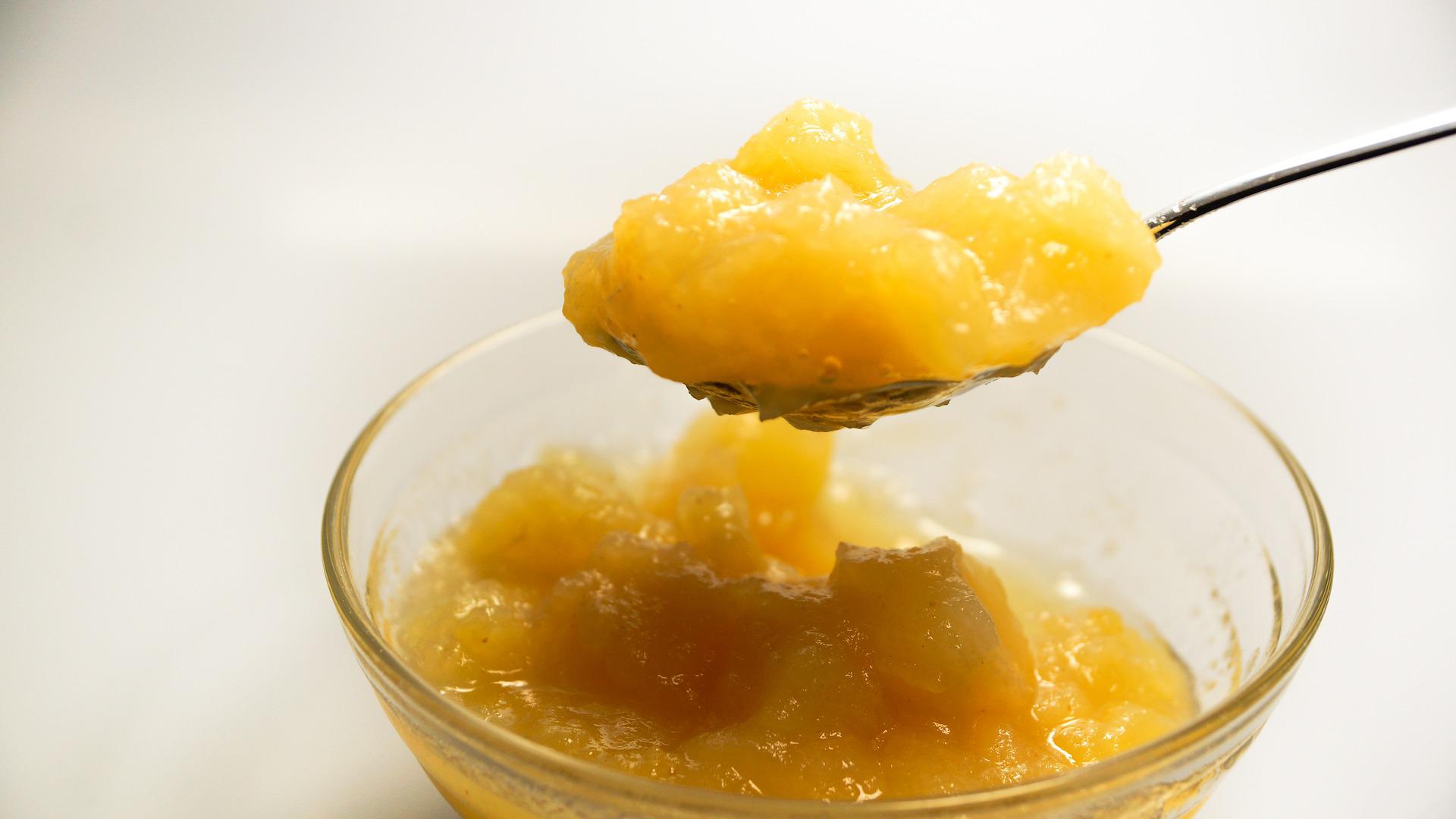 Cuillère remontant une compote de pommes maison au dessus d'un bol en verre posé sur fond blanc