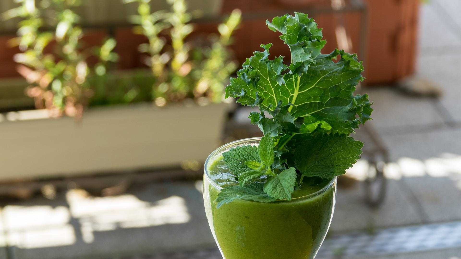 Smoothie vert servi en verre à pied décoré d'une feuille de chou kale et de menthe fraîche