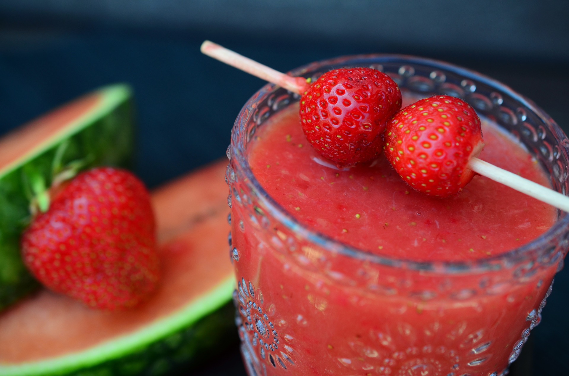 Gros plan sur un verre de smoothie épais à la fraise et à la pastèque, décoré de deux fraises fraîches sur un pique